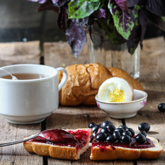 Breakfast: a sandwich with black currant berries, jam, eggs, basil and tea