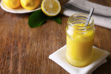 Glass jar with delicious lemon curd on wooden table
