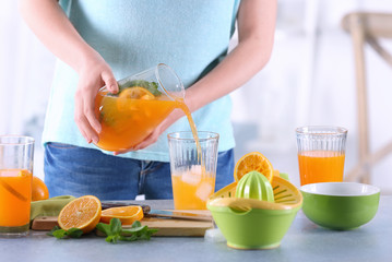 Woman pouring orange lemonade into glass in kitchen