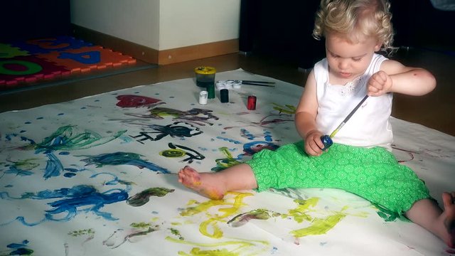 toddler boy with paintbrush and paints on floor