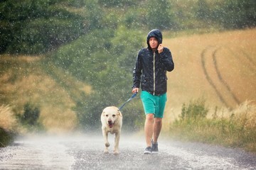 Man with dog in heavy rain - obrazy, fototapety, plakaty