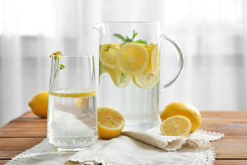 Jug and glass with refreshing lemon water on wooden table