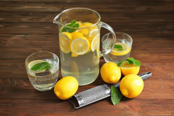 Jug and glasses with refreshing lemon water on wooden table
