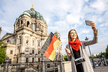 Young woman tourist making selfie with german flag in front of the famous cathedral in Berlin city
