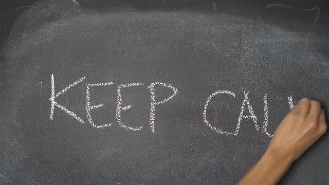 Woman's hand writing "KEEP CALM" with white chalk on blackboard