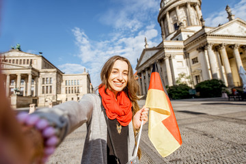 Obraz premium Young woman tourist making selfie photo with german flag on the French church and Opera house background in Berlin