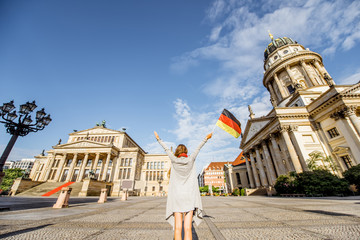 Obraz premium Young woman tourist standing back with german flag on the Gendarmen square with French church and Opera house on the background in Berlin