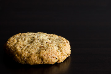 Single oatmeal cookie, healthy dessert, on dark background. Copy space