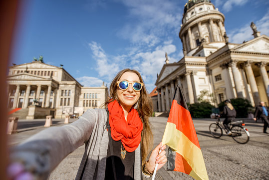 Young woman tourist making selfie photo with german flag on the French church and Opera house background in Berlin