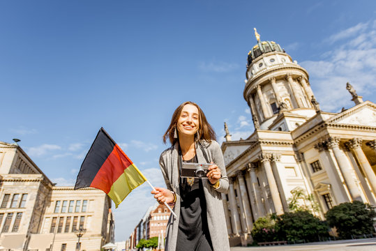 Young woman tourist standing with photo camera on the Gendarmen square with French church and Opera house on the background in Berlin