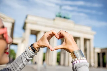 Tuinposter Young woman tourist making heart shape with hands in front of the famous Brandenburg gates in Berlin © rh2010