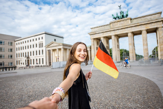 Young woman tourist walking with german flag to the famous Brandenburg gates in Berlin. Follow me concept