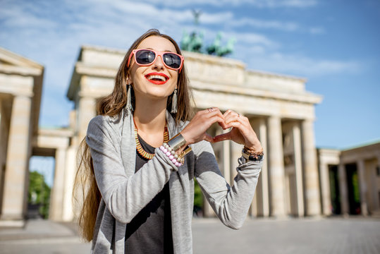 Young woman tourist making heart shape with hands in front of the famous Brandenburg gates in Berlin