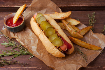 Fast food, hot dog with cucumber and onions, french fries on wooden background