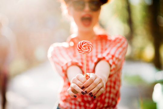 Sexy pinup girl holds out a hands with lollipop