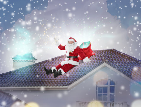 Santa Claus with bag sitting on roof of house. Christmas and New Year 2018 celebration