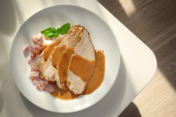 Plate with delicious sliced turkey and sauce on light table