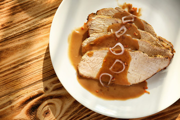 Plate with delicious sliced turkey and sauce on wooden table