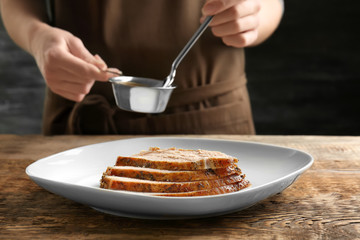 Tasty sliced turkey on plate and chef with gravy in small saucepan at table