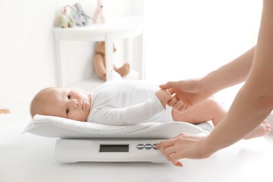 Mother weighting baby on scales in room