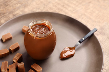 Glass jar with tasty caramel sauce on table