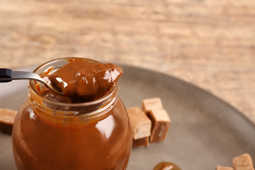 Glass jar with tasty caramel sauce and spoon on table