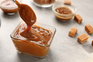 Glass bowl with tasty caramel sauce and spoon on table
