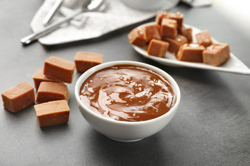Bowl with tasty caramel sauce and candies on table