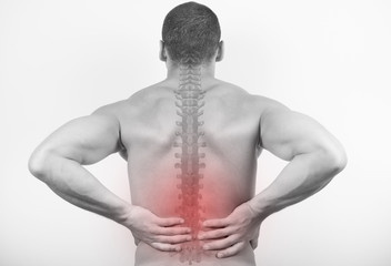 Rear view of a young man holding his back in pain, isolated on white background. Lower back pain. Shirtless man touching his back for the pain.
