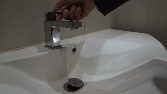 Male hand opening tap in bathroom, no water supply due to utility arrears