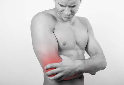 Front view of a young man holding his elbow in pain, isolated on white background. Lower arm pain. Shirtless man touching his elbow for the pain.