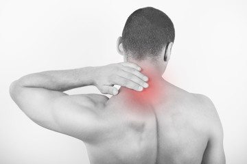 Rear view of a young man holding his neck in pain, isolated on white background. Lower neck pain. Shirtless man touching his neck for the pain.
