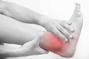 Close up view of a young man holding his ankle in pain, isolated on white background. Lower leg pain. Young man touching his ankle for the pain. Red inflammation effect.