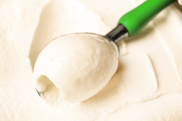 Tasty vanilla ice cream scooped out of container with utensil