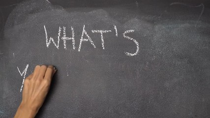 Woman's hand writing question "WHAT'S YOUR NAME?" with white chalk on blackboard