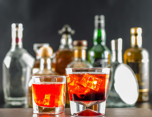 Colorful drink on the background of bottles in original shapes, cocktail drink with ice cubes