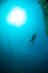Obraz na płótnie Canvas Scuba Divers, silhouettes against sunburst, in the ocean beside coral reef