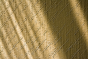 Texture from embossed stucco plaster lit by sunlight with playful shadows. Close-up of beige wall in retro style with pattern from diagonal scratches. Pleasing background with cheerful light stripes.