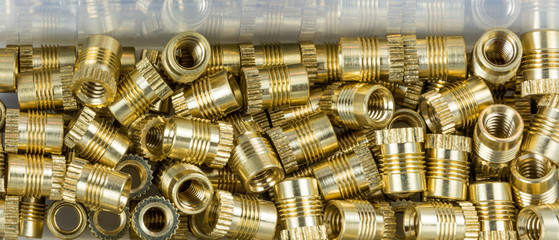 Threaded inserts close-up with mirroring in box. Decorative glossy thread bushings. Pile of small metallic fasteners in golden color. Idea of construction, build, assembly, hardware, store, industry.