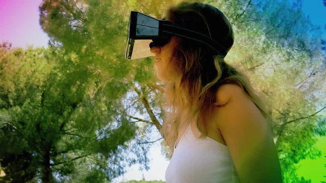 A woman in a park, wearing a virtual reality headset, exploring the imaginary surroundings with wide gestures. Larger-than-life coloring.

