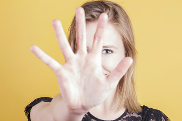 Blonde woman covering with her face with her hands, smiling. Over a yellow background. Studio shot.