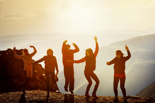 Happy friends dancing on sunset mountain