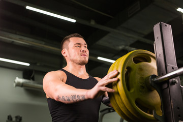 Young sportsman preparing his barbell by twisting power disk in.