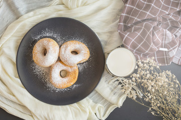 Sugary donuts on a black plate and glass of milk on a dark table background. in a windows light. Breakfast concept
