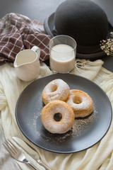 Sugary donuts on a black plate and glass of milk on a dark table background. in a windows light. Breakfast concept