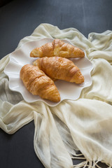Freshly baked croissants on a white plate on a dark table background. in a windows light. Breakfast concept