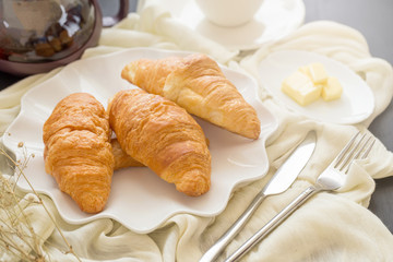 Freshly baked croissants and cup of tea on a white plate on a dark table background. in a windows light. Breakfast concept