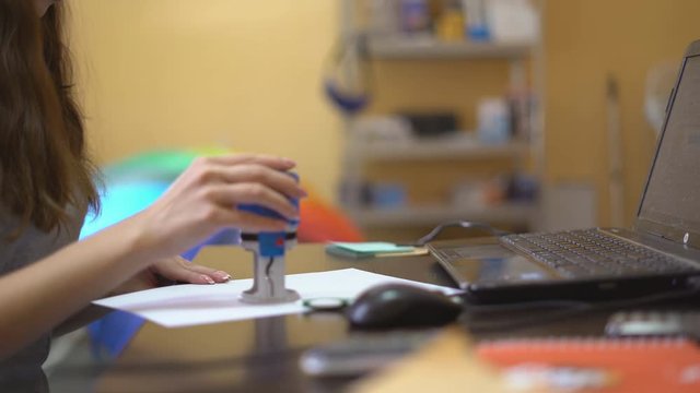 Young woman working in office with papers. Deaet approval by stapping with a seal on paper.