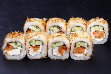 Appetizing fresh sushi roll with omelet in dried tuna flakes served on black slate, close up. Japanese healthy seafood.