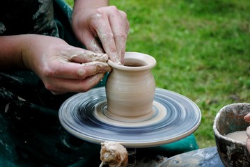 Potter's hands guiding child's hands to help him to work with the pottery wheel
